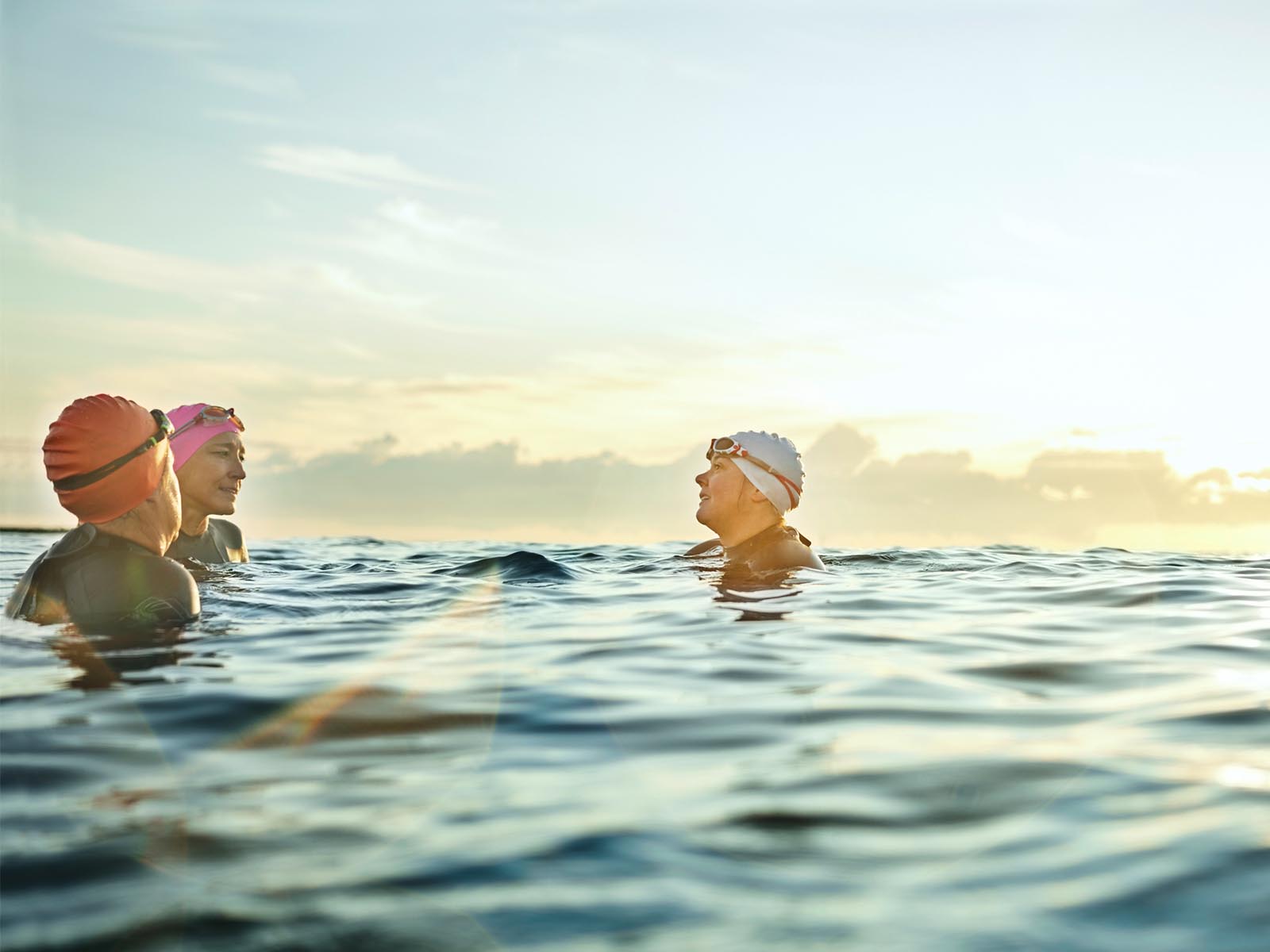 3 swimmers wearing caps and goggles talking in the sea